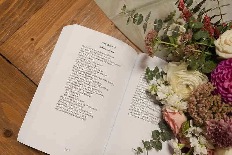 An open book of ceremony words beside a bouquet on a wooden table