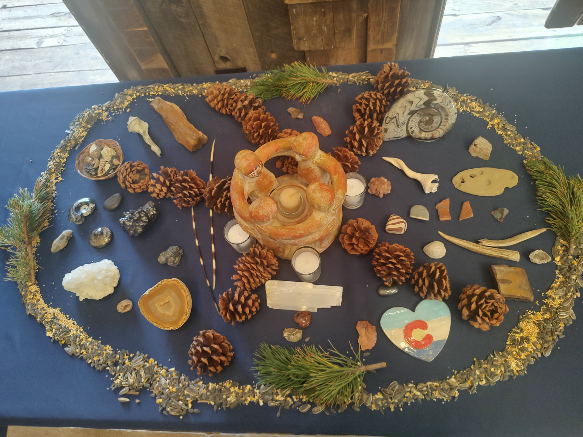 An altar of pine cones, stones and shells ringed with birdseed around a clay circle of friends holding hands
